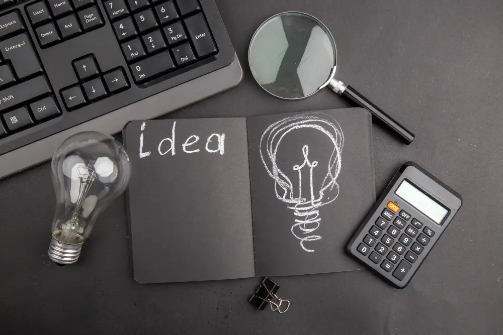 Desk scene with notebook, light bulb sketch, magnifying glass, keyboard, and calculator representing ideas and insights.