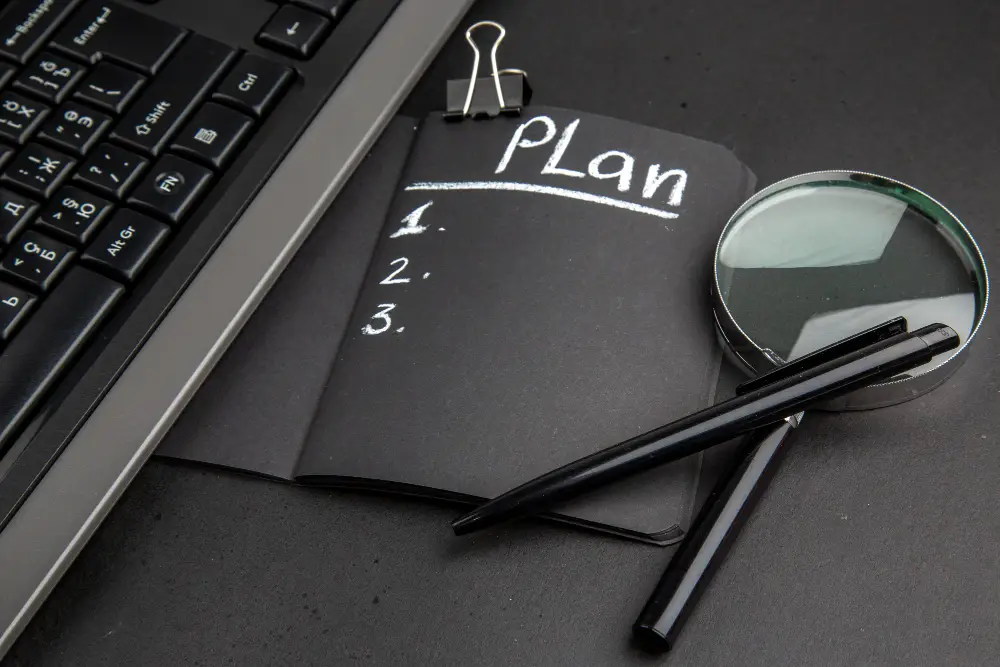 Notebook with plan checklist, laptop keyboard, pens, and magnifying glass representing business planning and strategy.